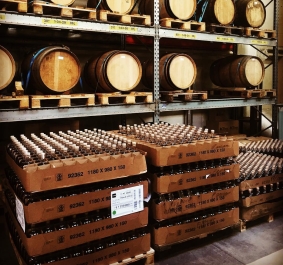 Holzfässer und Getränkekartons in einem Lagerregal gestapelt.