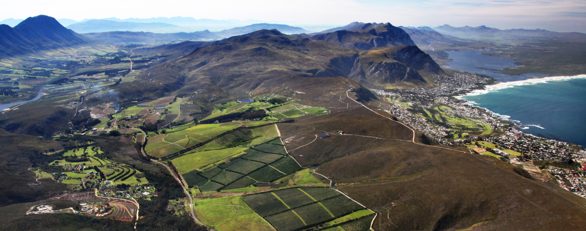 Luftaufnahme von grünen Feldern, Bergen und Küstenlinien mit blauem Meer im Hintergrund.