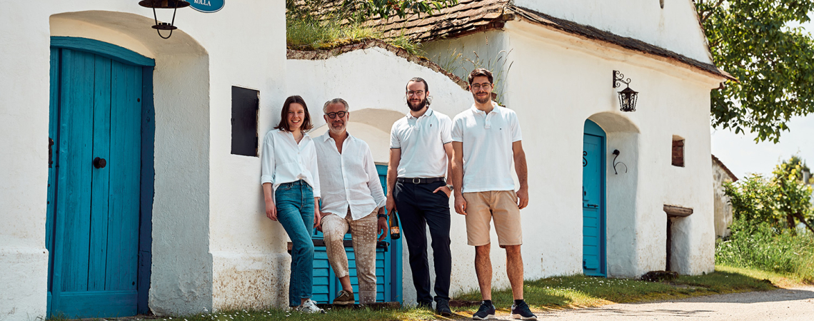 Vier Personen vor weißem Gebäude mit blauen Türen, sonnige ländliche Umgebung.