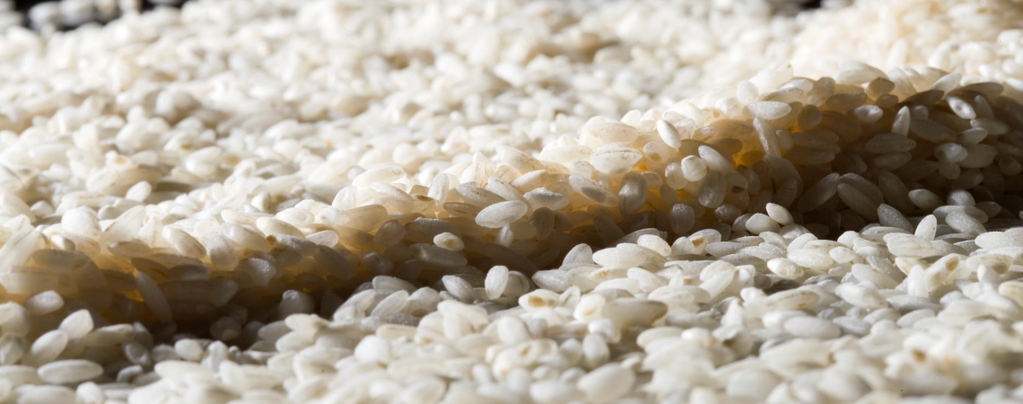 Nahaufnahme von weißem, ungekochtem Reis auf schwarzem Hintergrund.