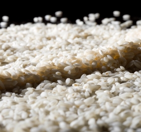 Nahaufnahme von weißem, ungekochtem Reis auf schwarzem Hintergrund.