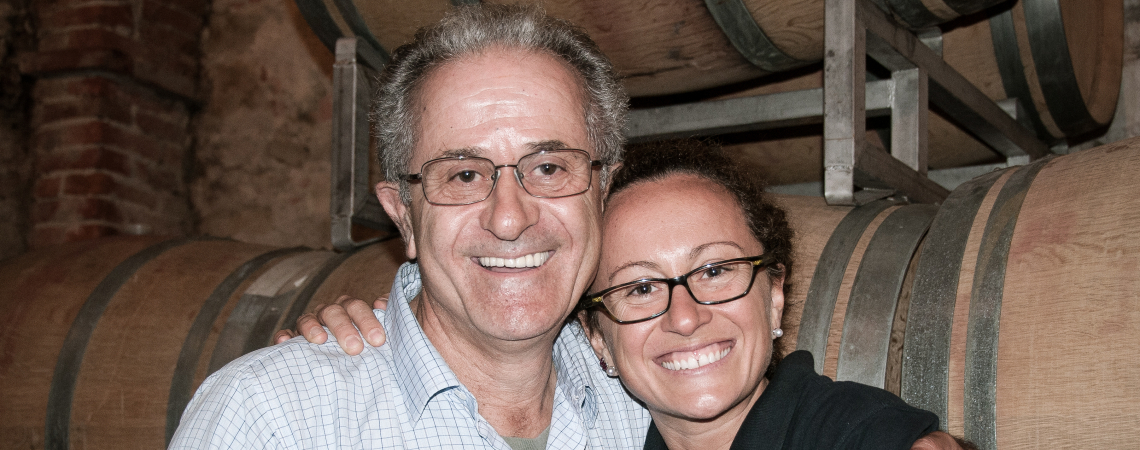 Zwei lachende Personen vor Weinfässern in einem Weinkeller.