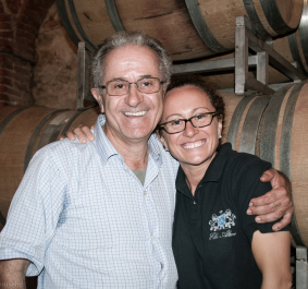 Zwei lachende Personen vor Weinfässern in einem Weinkeller.