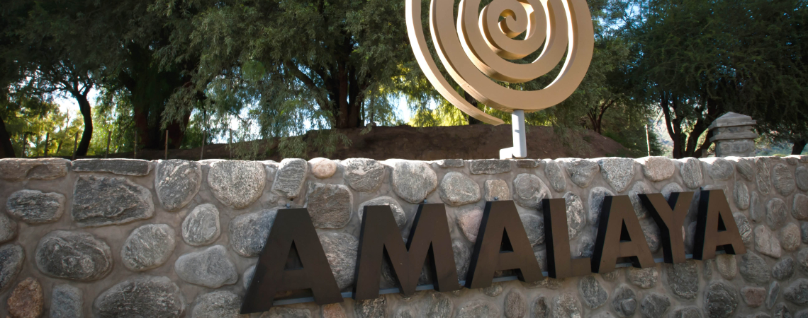 Steinmauer mit großem, goldenen Spiralsymbol, umgeben von grünen Bäumen.