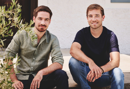 Zwei Männer sitzen auf einer Betonstufe, umgeben von grünen Pflanzen.