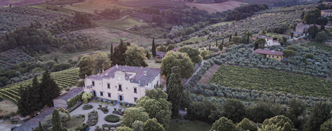 Luftaufnahme einer Villa inmitten von toskanischen Weinbergen und Hügeln bei Sonnenuntergang.