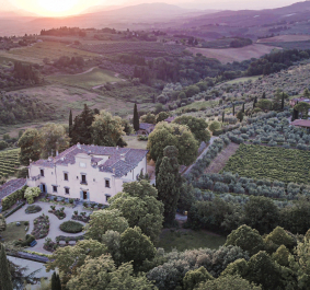 Luftaufnahme einer Villa inmitten von toskanischen Weinbergen und Hügeln bei Sonnenuntergang.