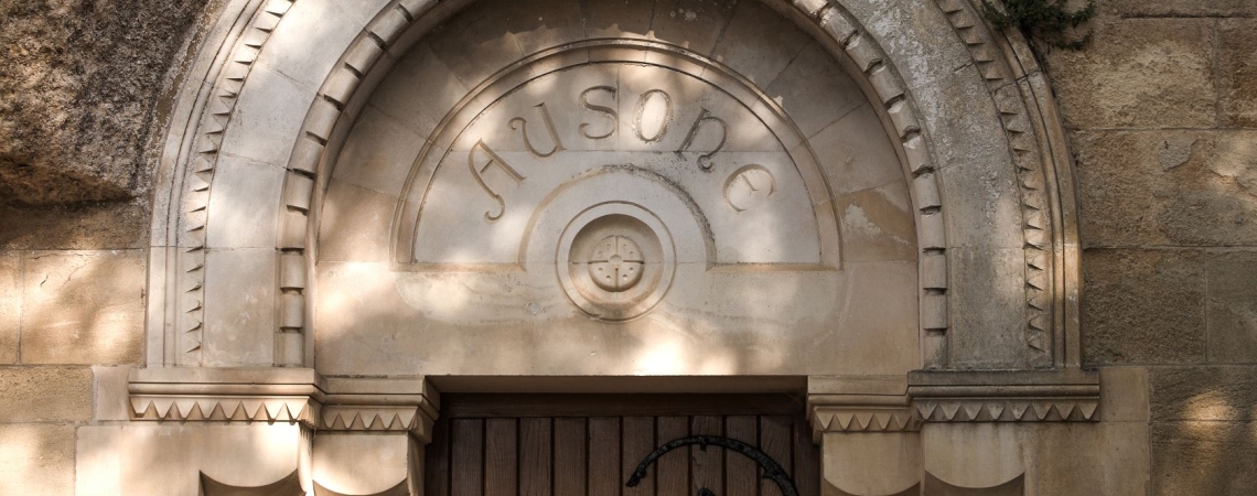 Steinernes, verziertes Rundbogenportal in Felswand integriert, mit schattigen Reliefs.