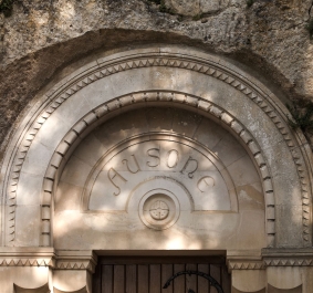 Steinernes, verziertes Rundbogenportal in Felswand integriert, mit schattigen Reliefs.