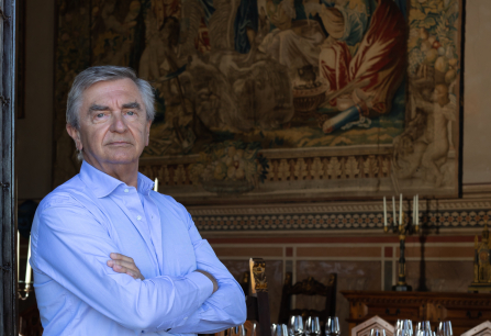 Eleganter Mann in blauem Hemd vor historischer Wandteppichkulisse in edlem Speisesaal.