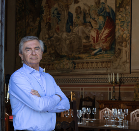 Eleganter Mann in blauem Hemd vor historischer Wandteppichkulisse in edlem Speisesaal.