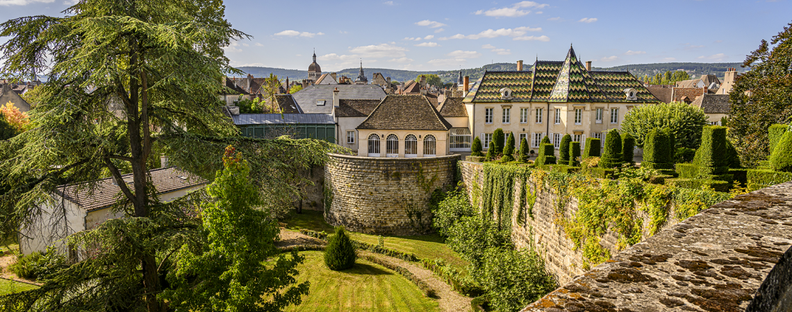 Schloss mit gepflegtem Garten, umgeben von Steinmauer, bei sonnigem Wetter.