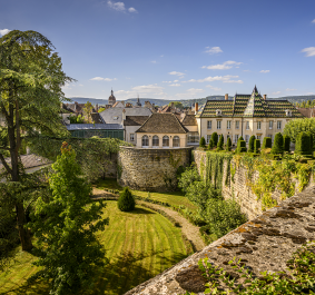 Schloss mit gepflegtem Garten, umgeben von Steinmauer, bei sonnigem Wetter.