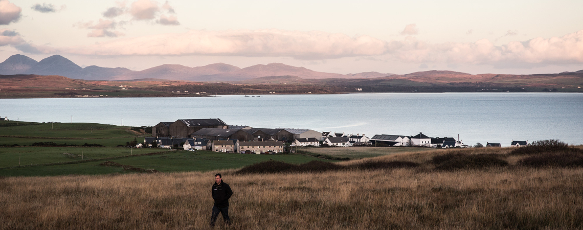 Weite Landschaft mit Blick auf ein Dorf am See und dahinterliegende Berge.