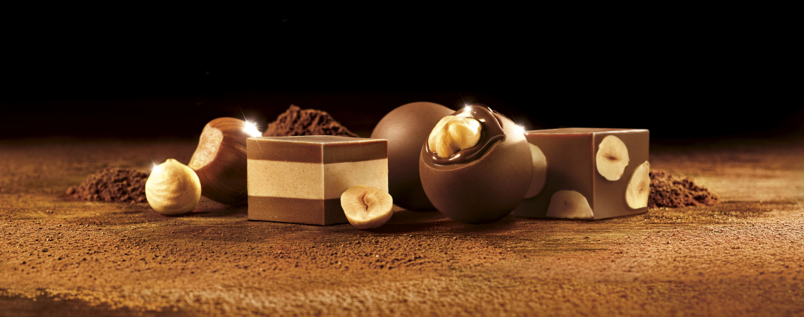 Pralinen und Schokoladenwürfel mit Haselnüssen vor dunklem Hintergrund auf Kakao.