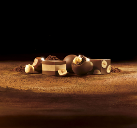 Pralinen und Schokoladenwürfel mit Haselnüssen vor dunklem Hintergrund auf Kakao.