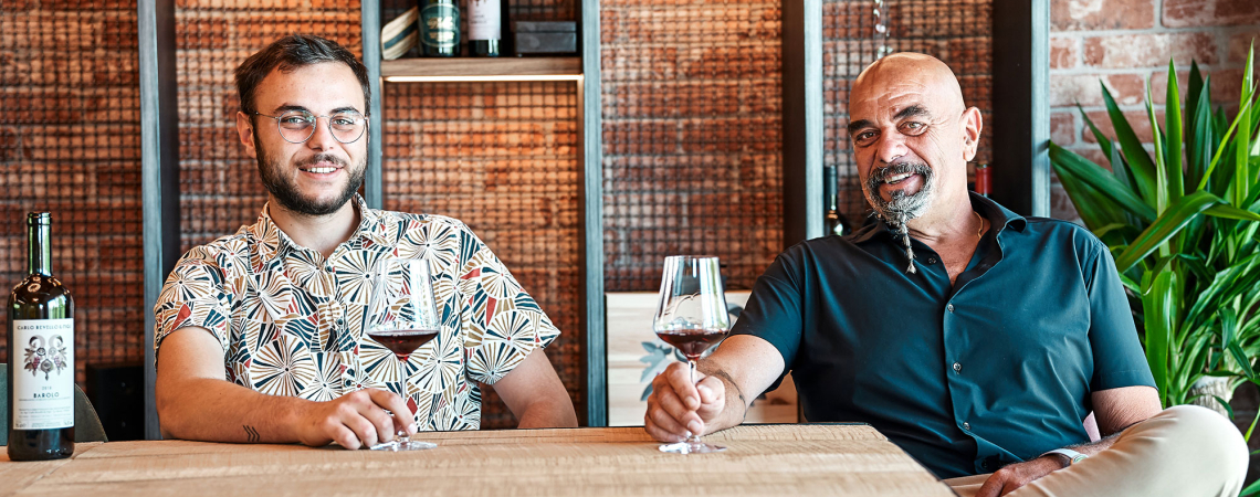 Zwei Männer sitzen mit Weingläsern an einem Tisch in gemütlichem Ambiente.