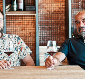 Zwei Männer sitzen mit Weingläsern an einem Tisch in gemütlichem Ambiente.