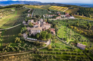 Luftaufnahme eines Dorfes mit umgebenden Weinbergen und Olivenhainen in Hügellandschaft.