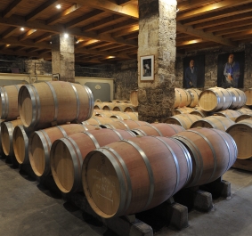 Weinkeller mit gestapelten Holzfässern auf Steinboden und gemauerten Wänden.