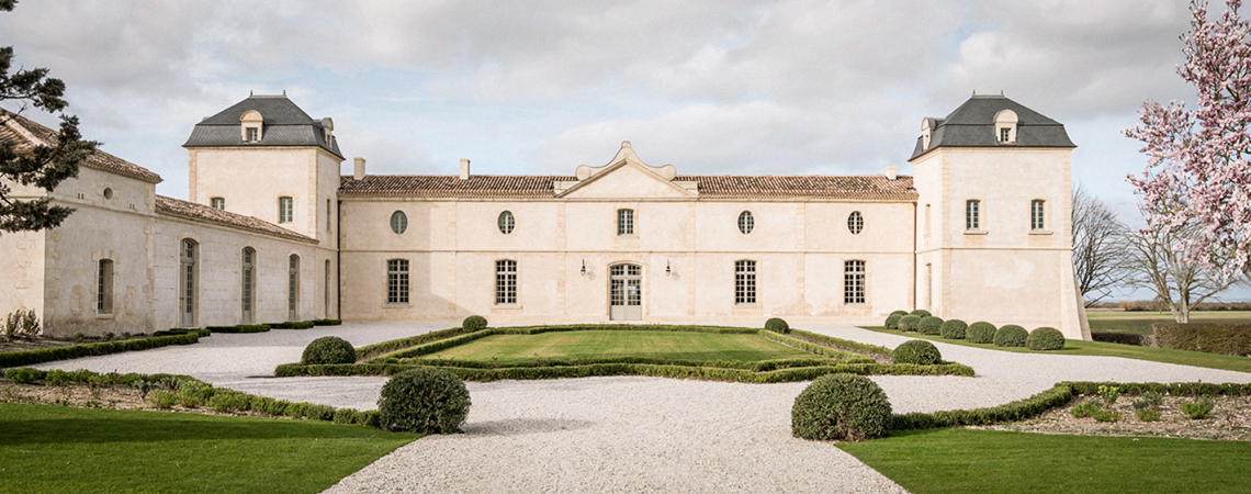 Helles, elegantes Schloss mit symmetrischer Fassade, zwei Türmen und gepflegten Gärten.