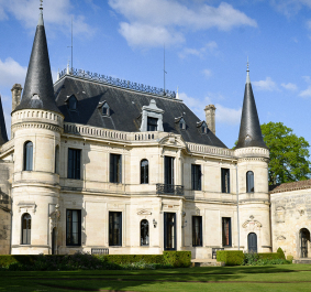 Prächtiges Schloss mit Türmen, zahlreichen Fenstern und gepflegtem Garten im Vordergrund.
