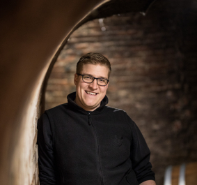 Mann in einer gewölbten, rustikalen Weinkellergasse, trägt dunkle Kleidung.