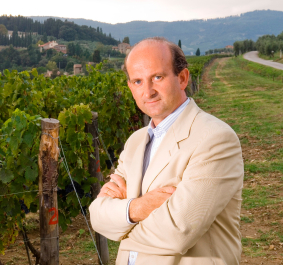 Mann in beigem Anzug vor grünen Weinreben und hügeliger Landschaft.
