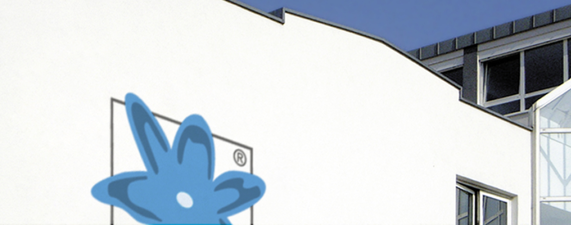 Weiße Gebäudeansicht mit blauem Logo und modernen Fenstern unter klarem Himmel.