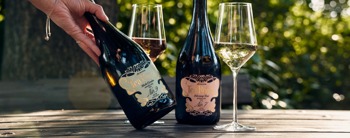 Zwei Sektflaschen und Gläser auf Holztisch im grünen Garten.