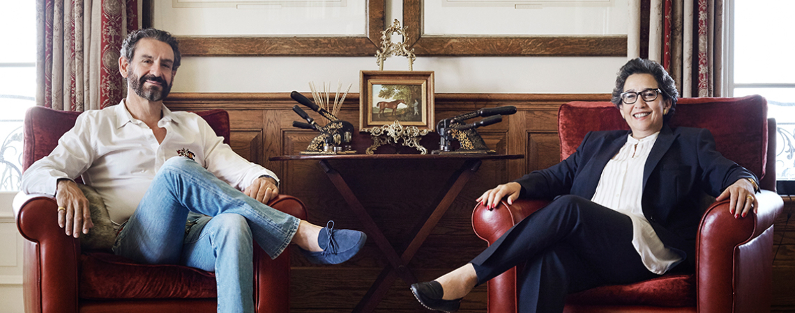 Zwei Personen sitzen auf roten Sesseln vor eleganter, holzgetäfelter Wand mit Kunstwerken.