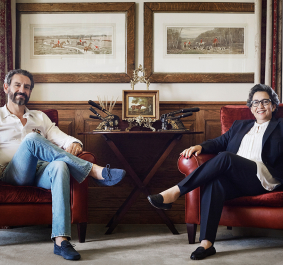 Zwei Personen sitzen auf roten Sesseln vor eleganter, holzgetäfelter Wand mit Kunstwerken.