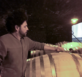 Person im Keller bei Holzfässern, gedämpfte Beleuchtung.