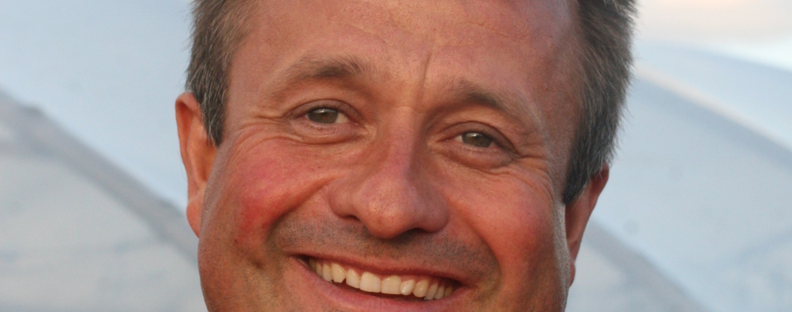 Mann in rotem Hemd hält kleine, unförmige Tomaten in der Hand und lächelt.