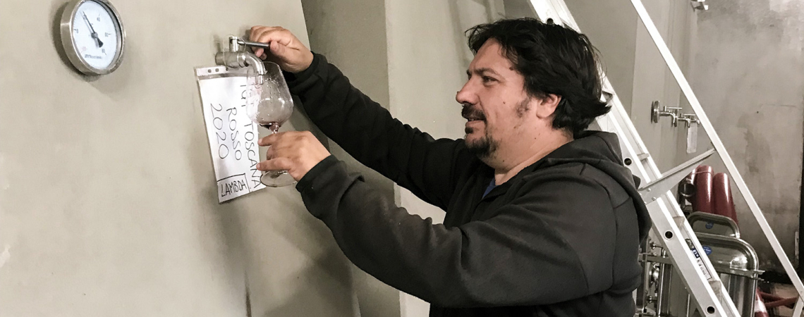 Mann zapft Weinprobe aus großem, rechteckigem Weintank in Keller.