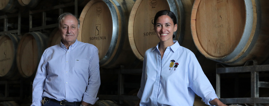 Zwei Personen posieren vor gestapelten Weinfässern in einem Weinkeller.