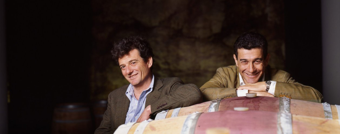 Zwei Männer lehnen an alten Weinfässern in einem dunklen Keller.