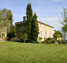 Großes, elegantes Landhaus aus Stein, umgeben von gepflegtem Rasen und hohen Bäumen.
