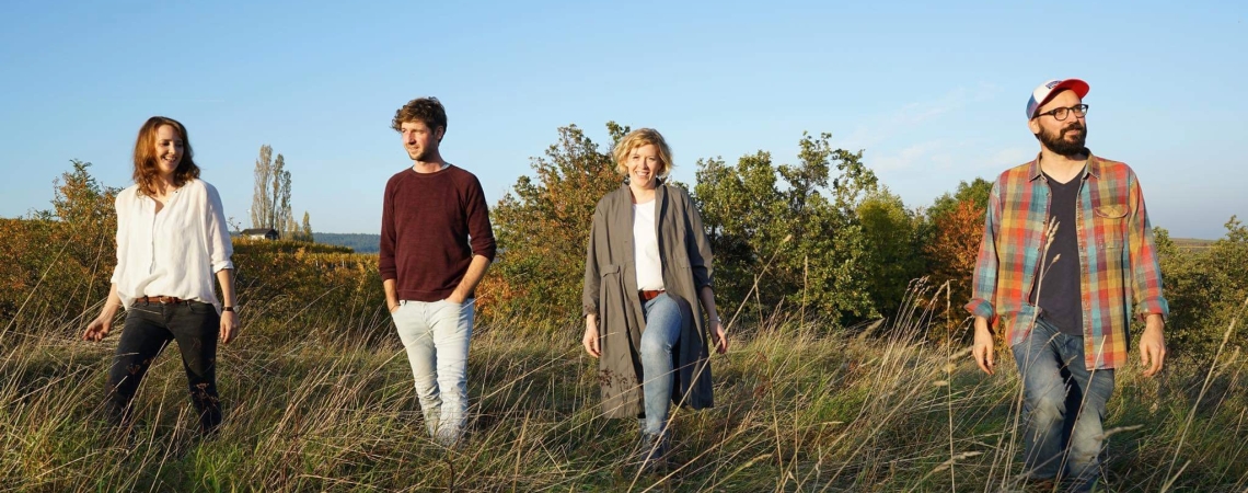 Vier Menschen spazieren durch eine herbstliche Wiese unter klarem Himmel.