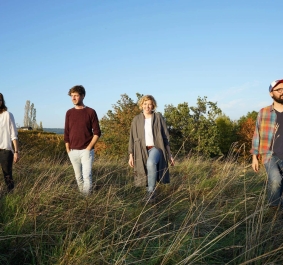 Vier Menschen spazieren durch eine herbstliche Wiese unter klarem Himmel.