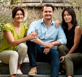 Drei Personen sitzen auf einer Treppe in einem grünen, natürlichen Gartenumfeld.