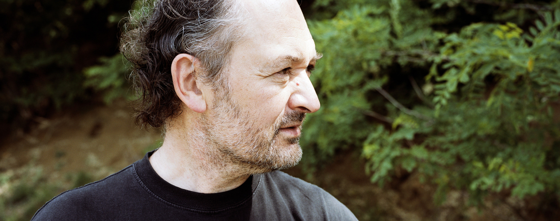 Mann in schwarzem T-Shirt mit Bart im Grünen stehend.