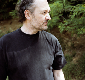 Mann in schwarzem T-Shirt mit Bart im Grünen stehend.