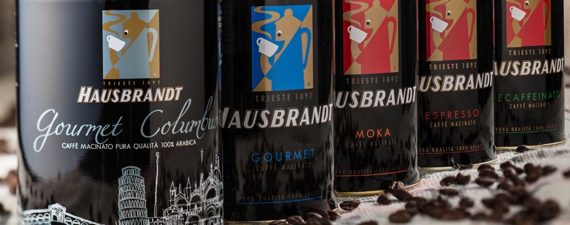 Fünf Kaffeedosen in Reihe mit unterschiedlichen Farben und Motiven, auf gestreuter Kaffeebohne.