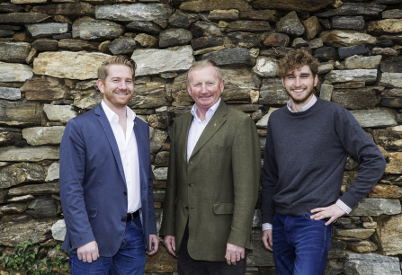 Drei Männer in Freizeitkleidung vor einer rustikalen Steinmauer.