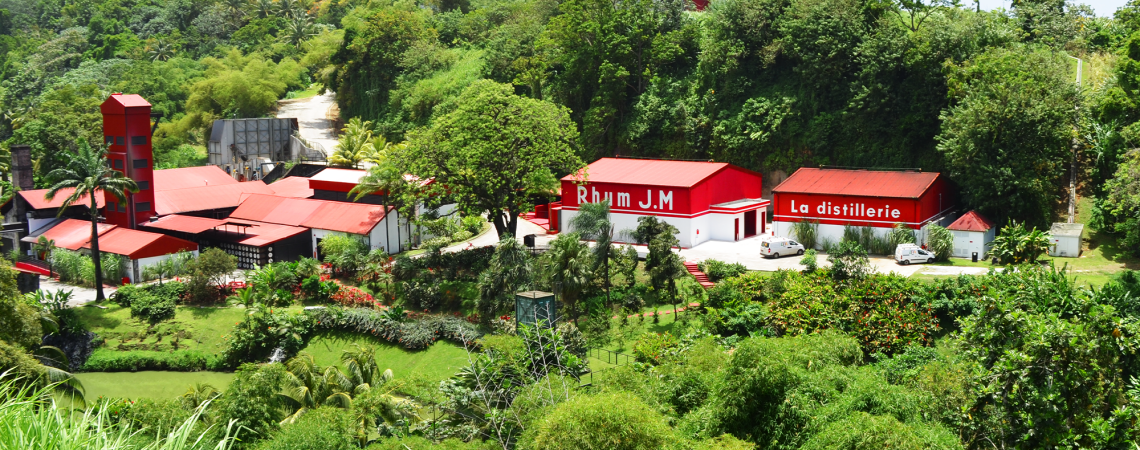 Rote Gebäude in üppiger, grüner, tropischer Landschaft mit blauem Himmel.