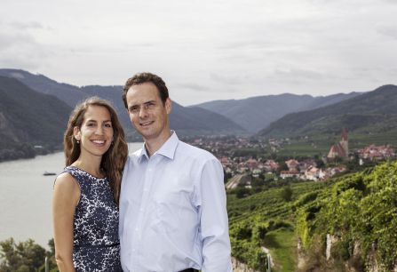 Paar vor malerischer Berglandschaft mit Fluss und Weinbergen im Hintergrund.