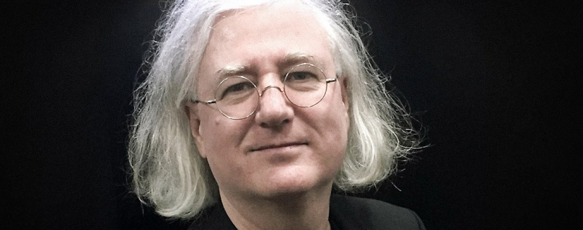 Älterer Mann mit weißem Haar und Brille vor schwarzem Hintergrund.