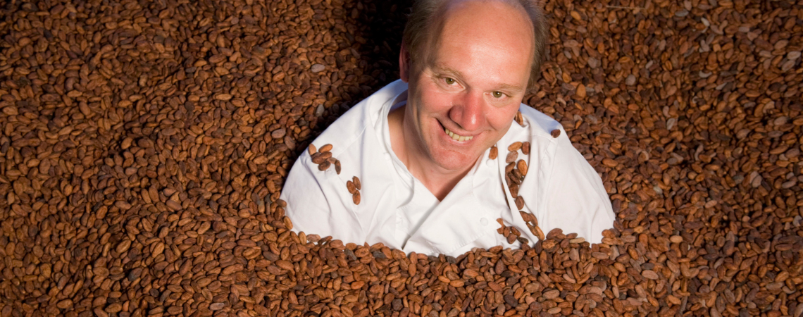 Mann in weißem Kittel, umgeben von vielen Kakaobohnen.