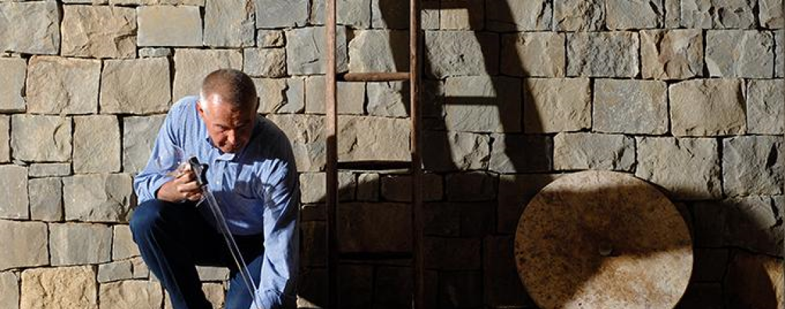 Mann öffnet metallenen Zugangsschacht vor Steinmauer und Leiter.